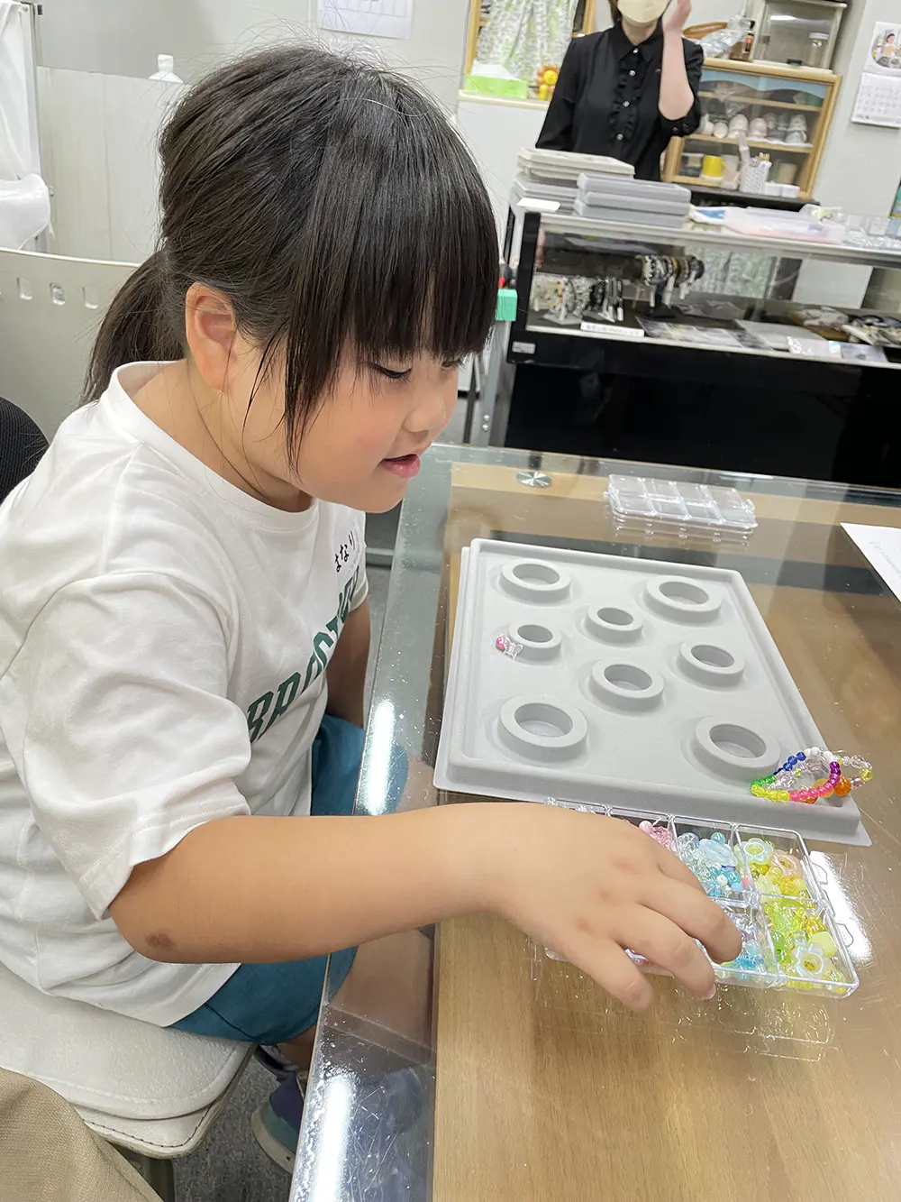 HANARI
始めに工場を見学しました。いろいろな機械があって、指輪を磨いたり石をつけたりしていて、難しそうだったけど大人になったらやってみたいなと思いました。その後ビーズでブレスレットを作り、たくさんの可愛いビーズを自分で選んで、並び方も考えてブレスレットを作り、楽しかったです。ブレスレットの包装も楽しかったです。お母さんがお客さんになって、レジもしました。お店の人に教えてもらいながらレジのボタンを押して緊張したけど、ちゃんとできて嬉しかったです。
また3年生になったらやってみたいです。